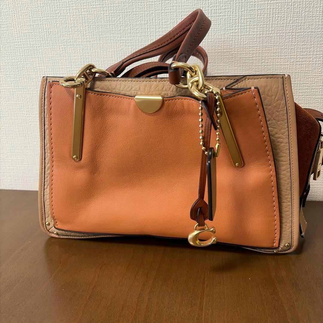 Front view of the COACH leather multicolor shoulder bag showing an orange front panel, beige trim, gold hardware, and a hanging charm.