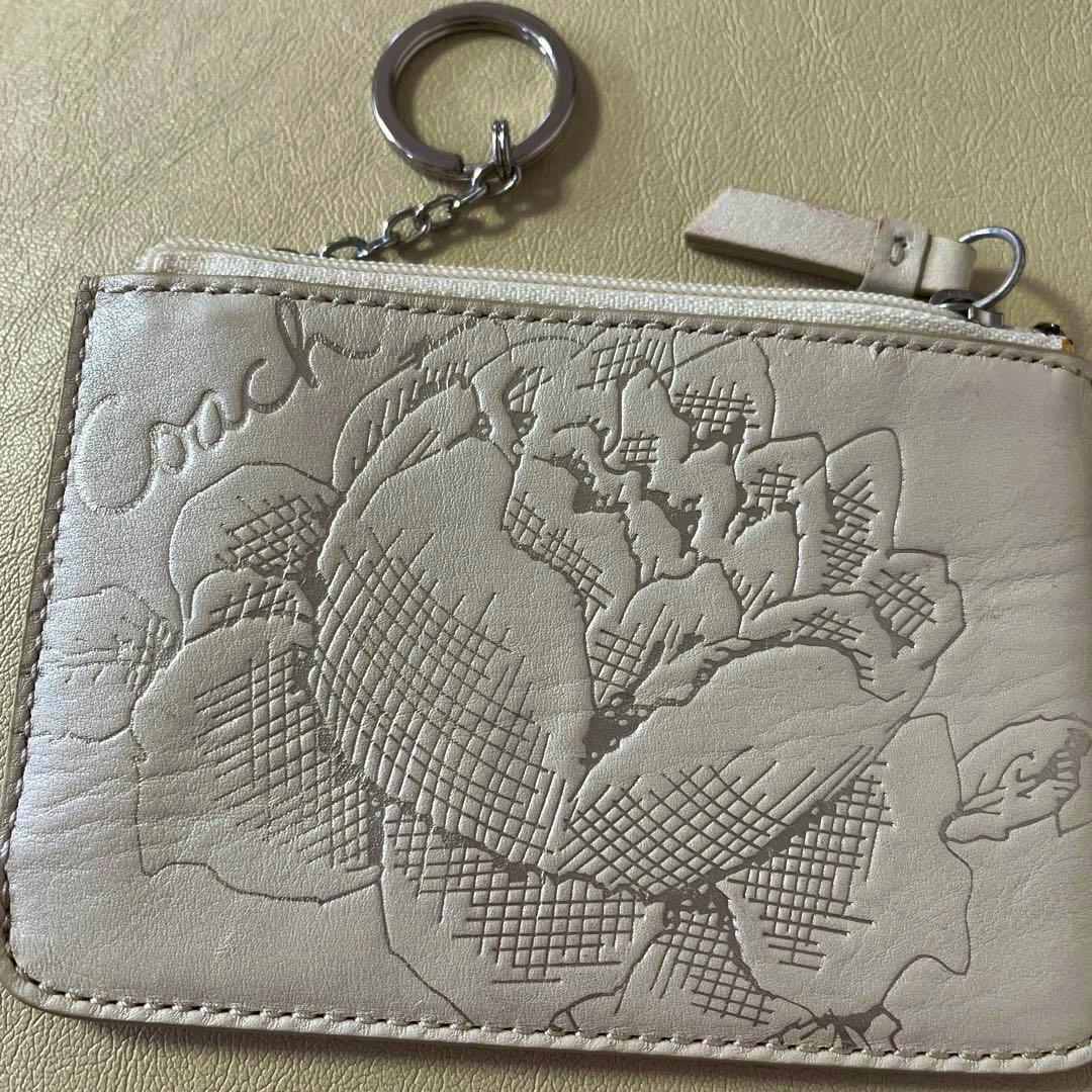 Cream leather Coach pass case with an embossed floral design, zipper, and attached key ring.
