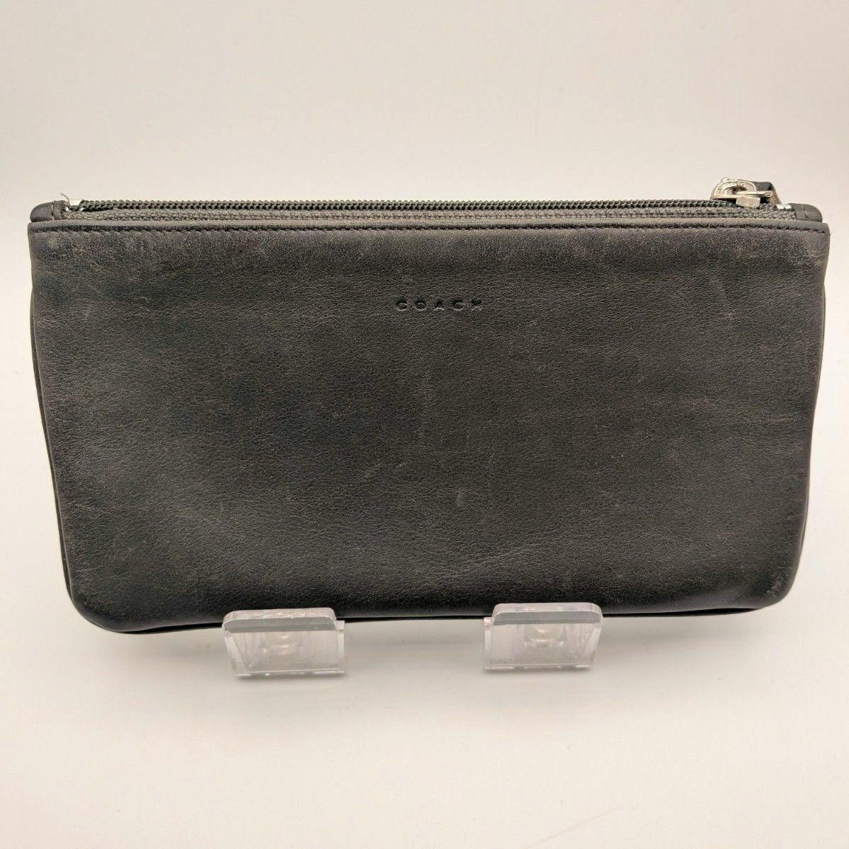 Front view of a black Coach leather pouch with a top zipper displayed on a clear stand.