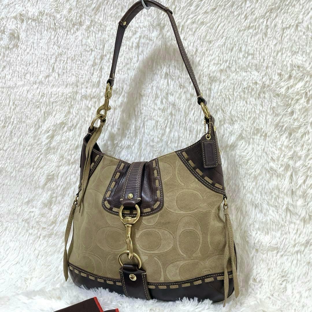 Beige COACH shoulder bag with brown leather trim, brass hardware, and embossed C pattern on a white fluffy background.