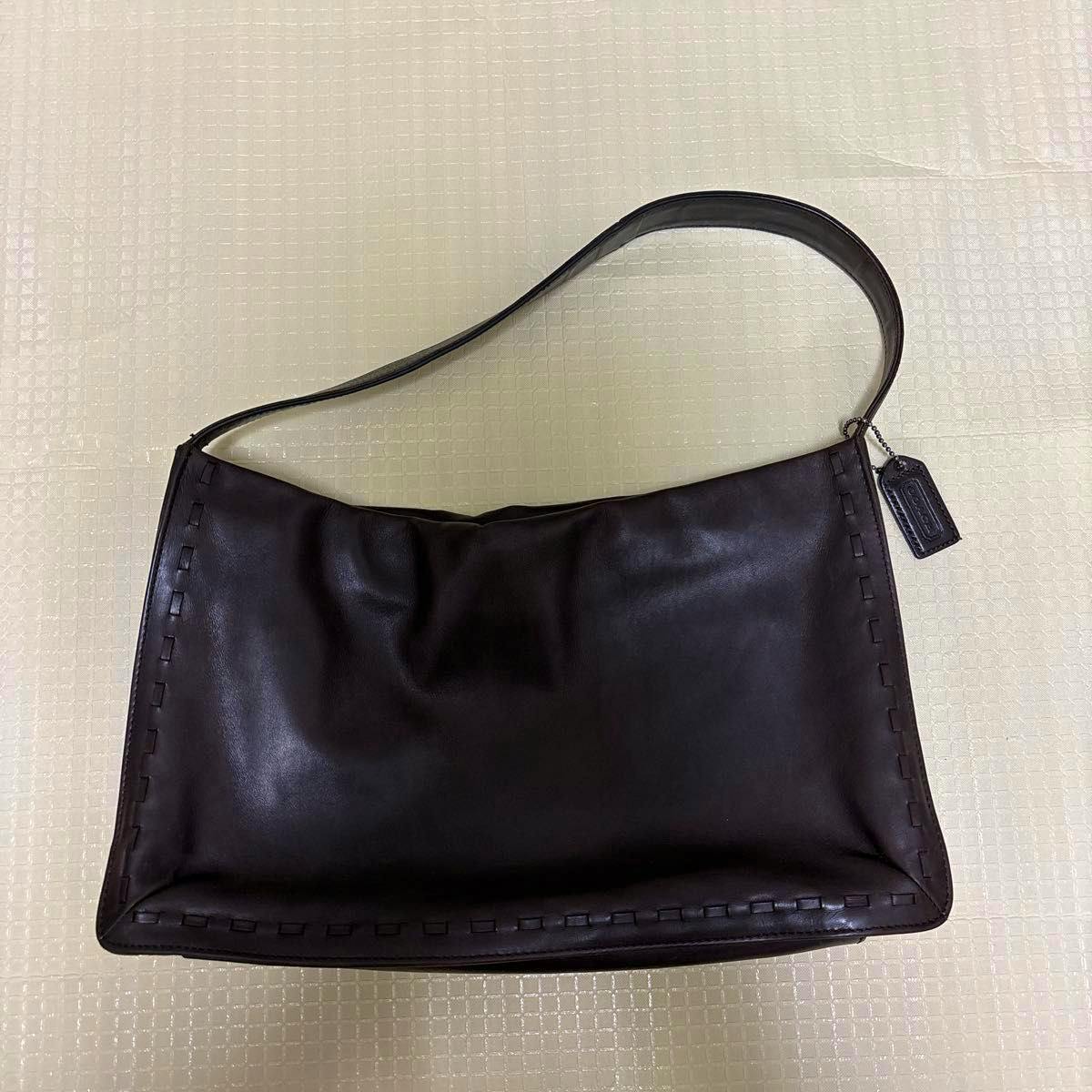Black COACH leather shoulder bag shown flat with a single shoulder strap and a hang tag.
