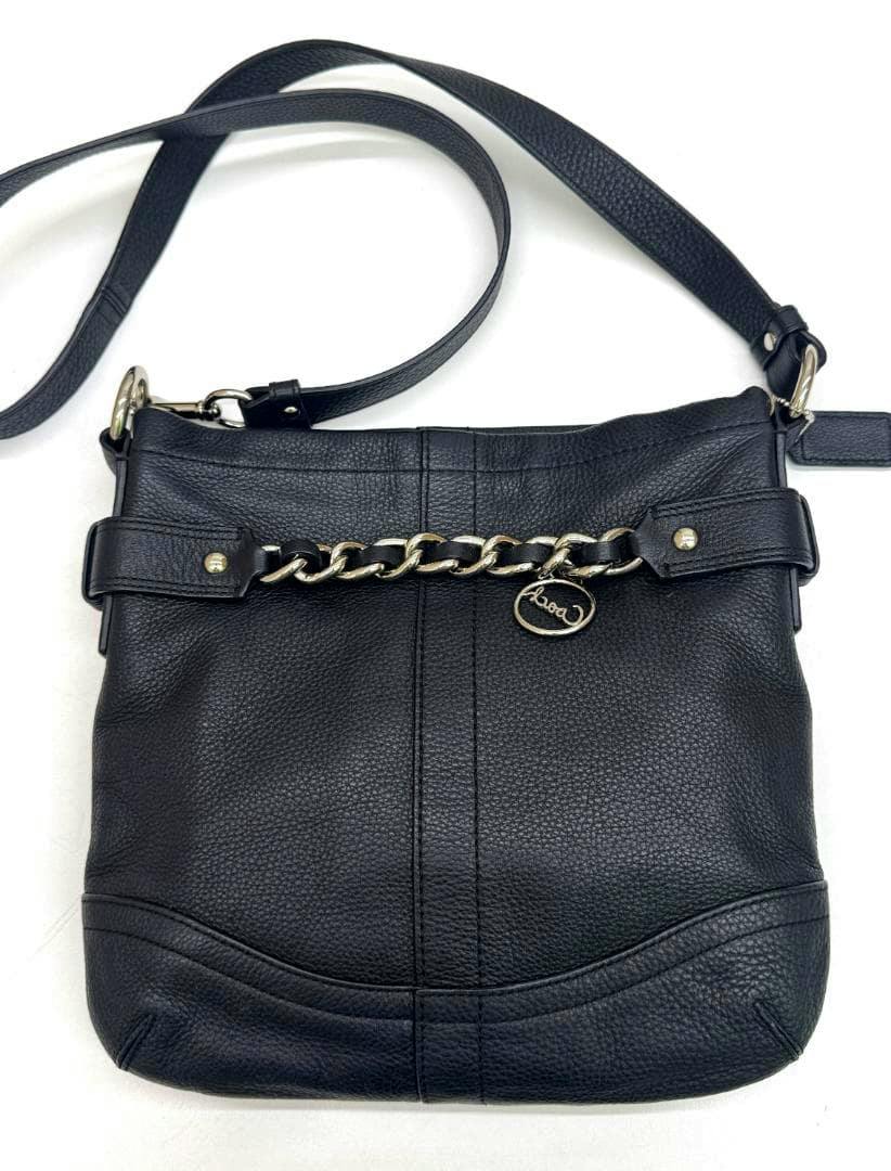 Black Coach cow leather shoulder bag with a chain-accent front and adjustable strap on a white background.