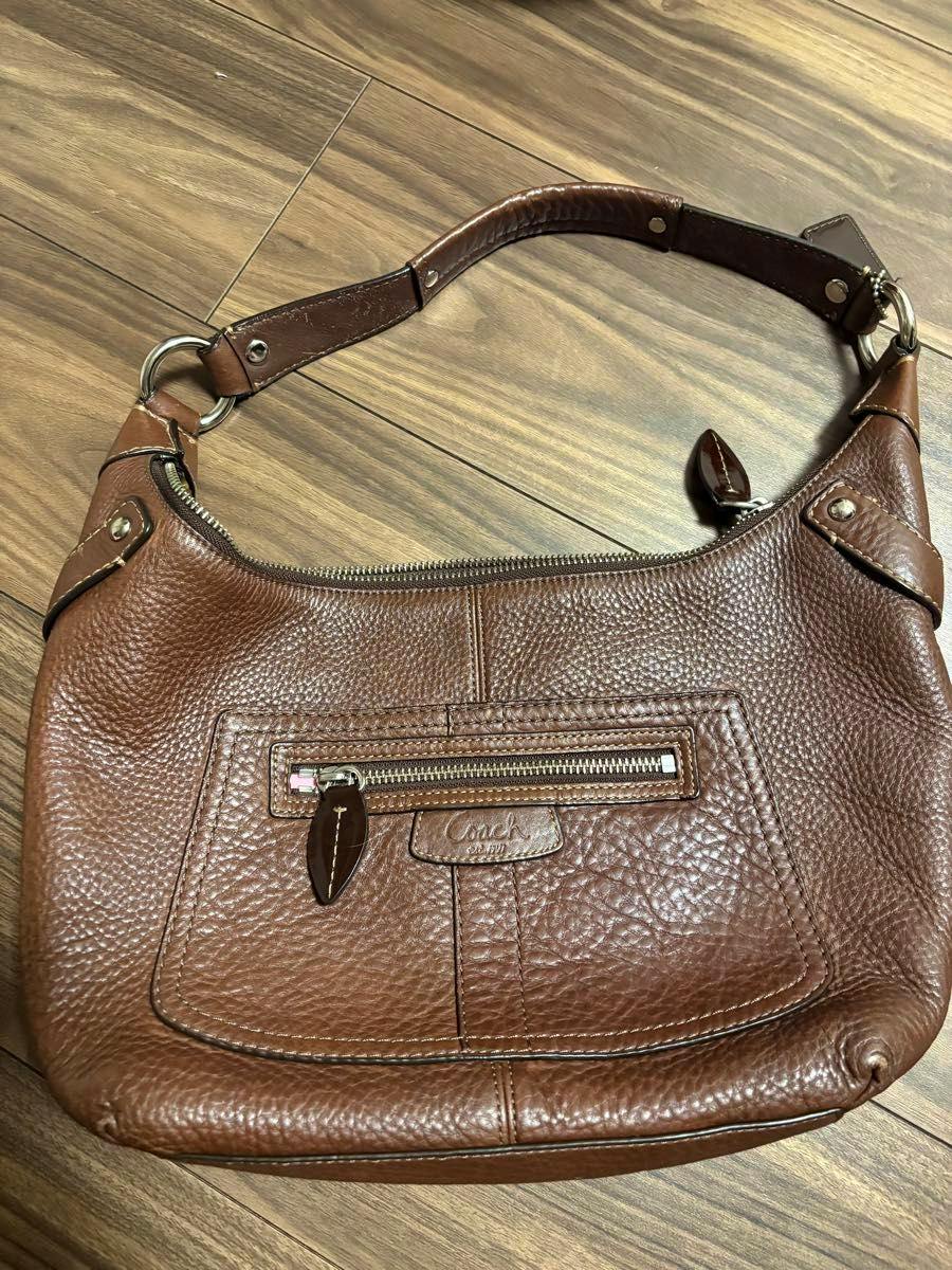 Brown Coach leather shoulder bag lying flat on a wood floor, showing the front pocket and shoulder strap.