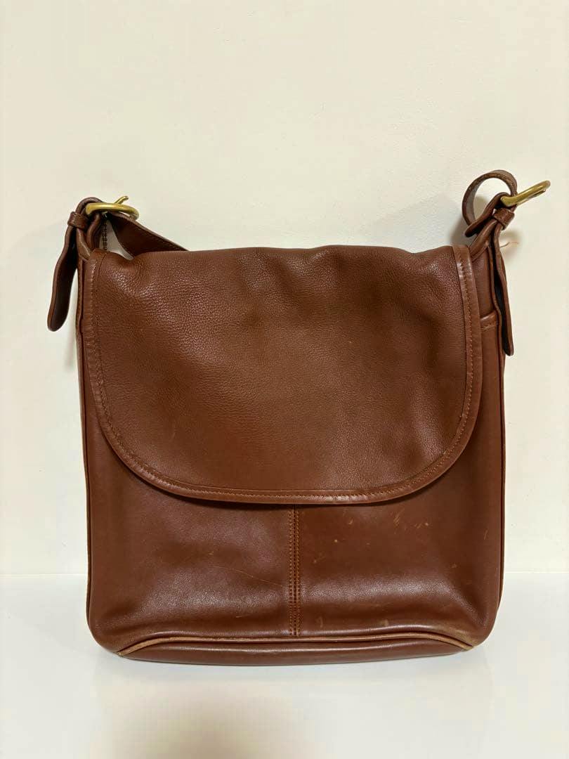 Brown leather Coach shoulder bag with a front flap displayed against a white background.