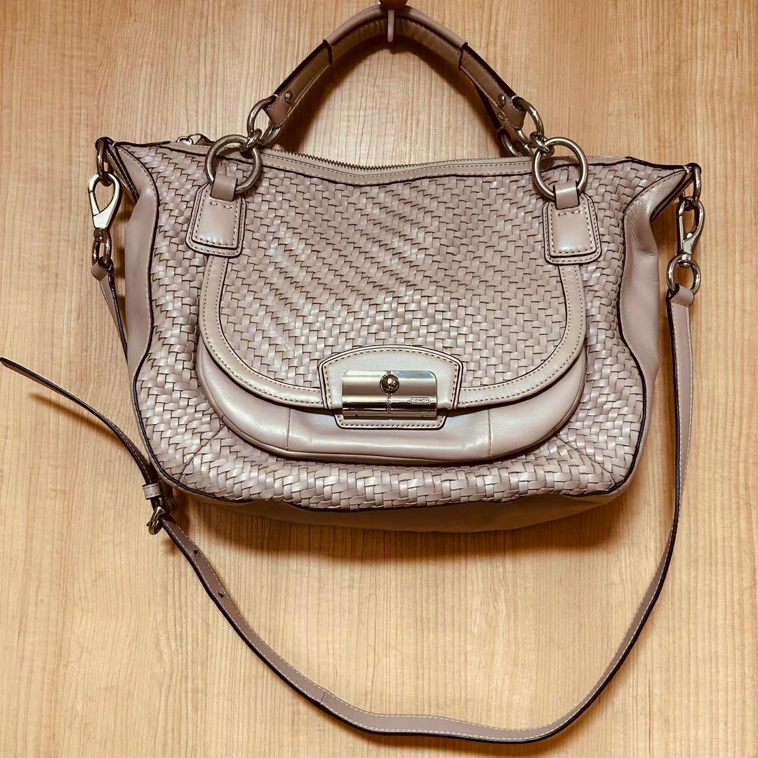 Pink-beige woven leather Coach shoulder bag laid flat on a wooden surface.