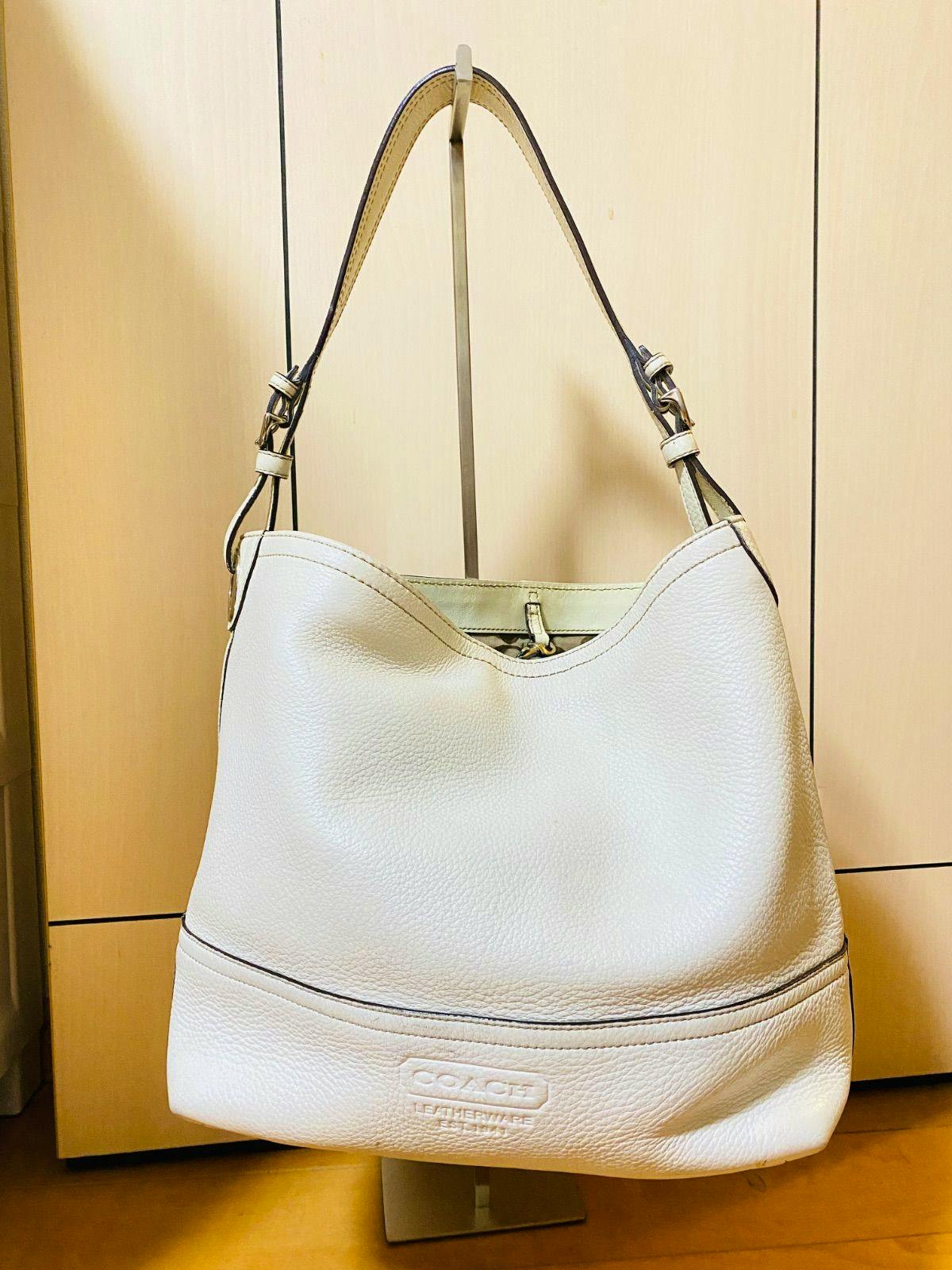 White Coach leather shoulder bag hanging on a stand showing the front and strap.