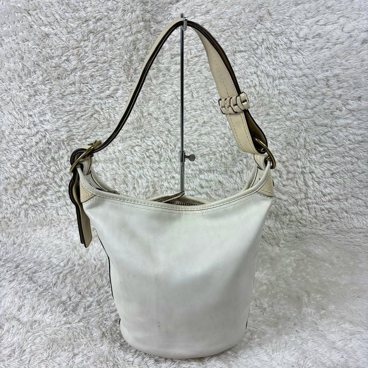 White Coach leather shoulder bag hanging on a metal display stand against a textured white background.