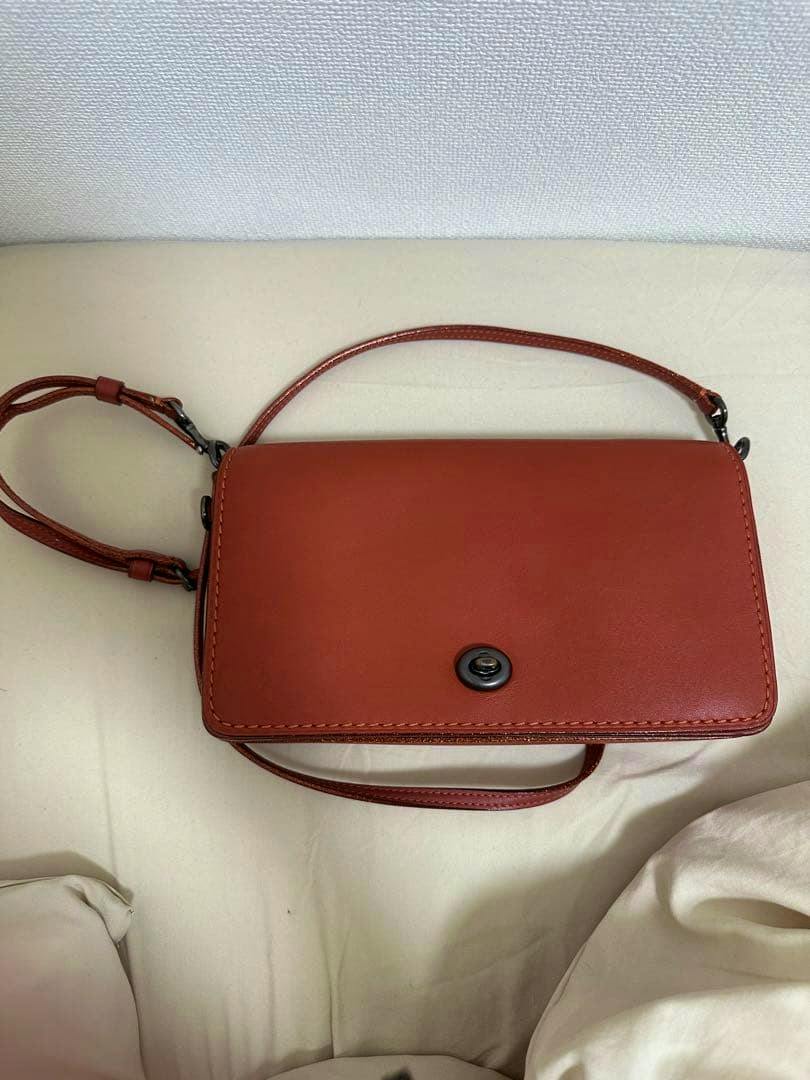 Red-brown leather COACH shoulder bag with a flap and turn-lock, lying flat with the strap visible.