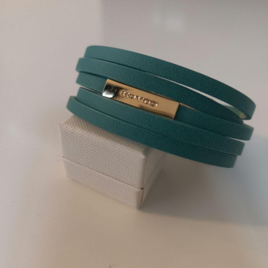 Emerald multi-strand leather COACH bracelet with a gold-tone rectangular clasp displayed on a small white box.