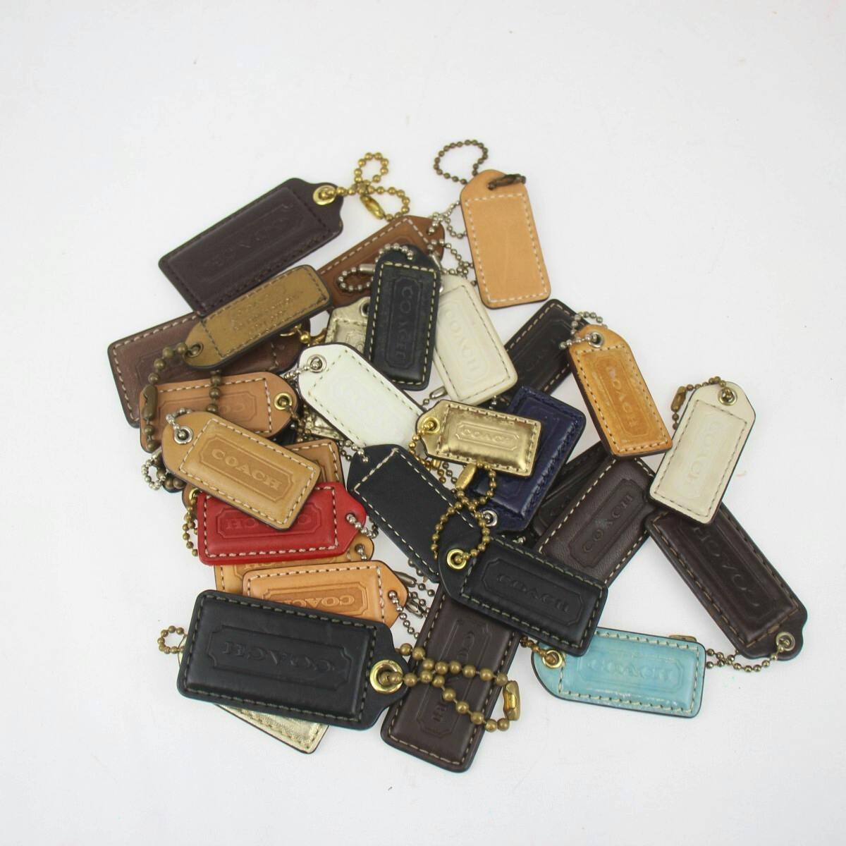 Pile of multi-colored COACH leather tag charms with ball chains on a white background.
