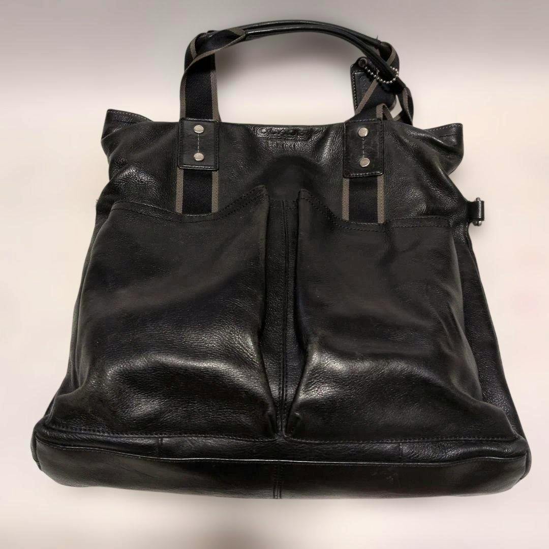 Black leather COACH tote bag photographed from the front showing two exterior pockets, two handles, and a center seam.