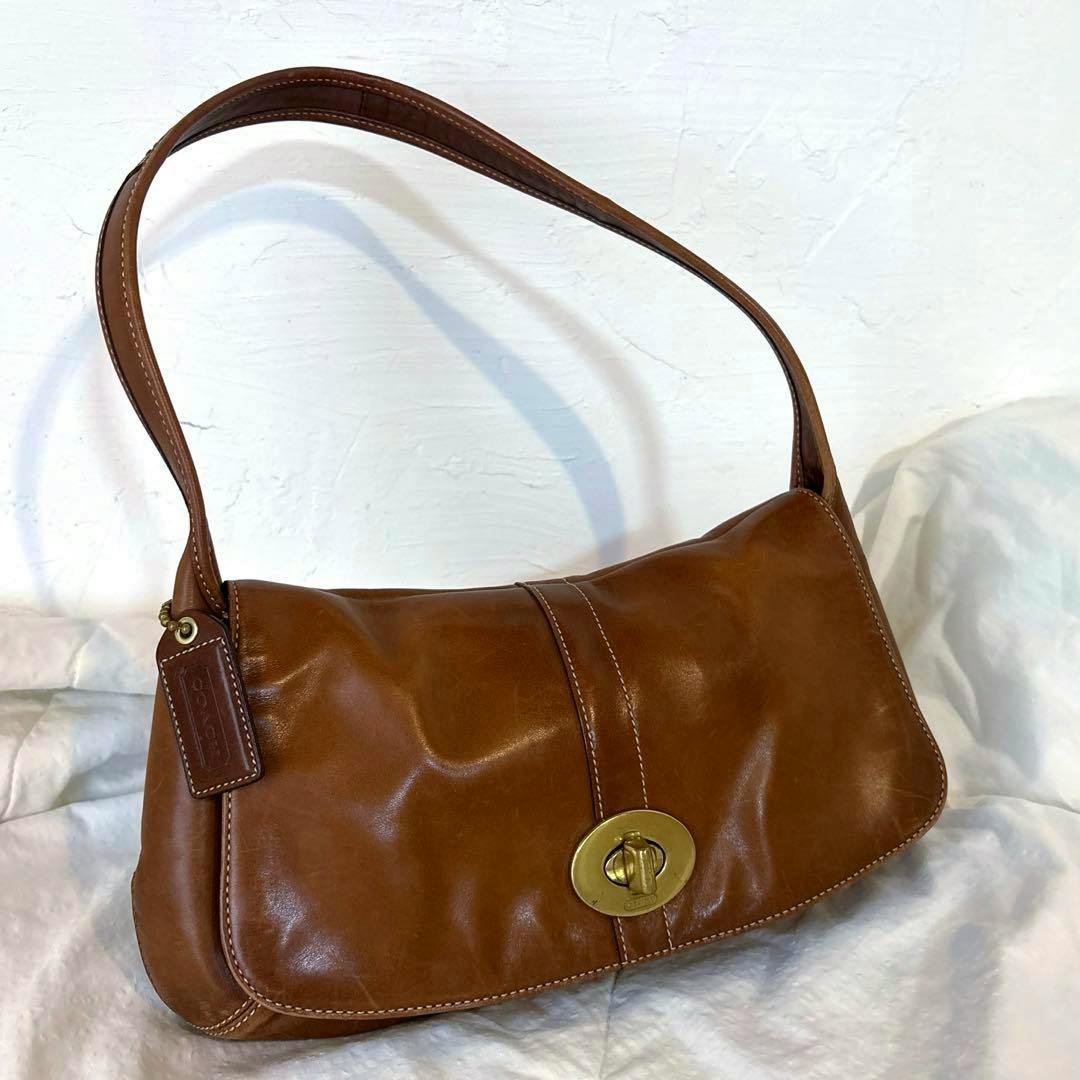 Brown COACH cow leather shoulder bag with one strap and a turnlock closure resting on a white background.