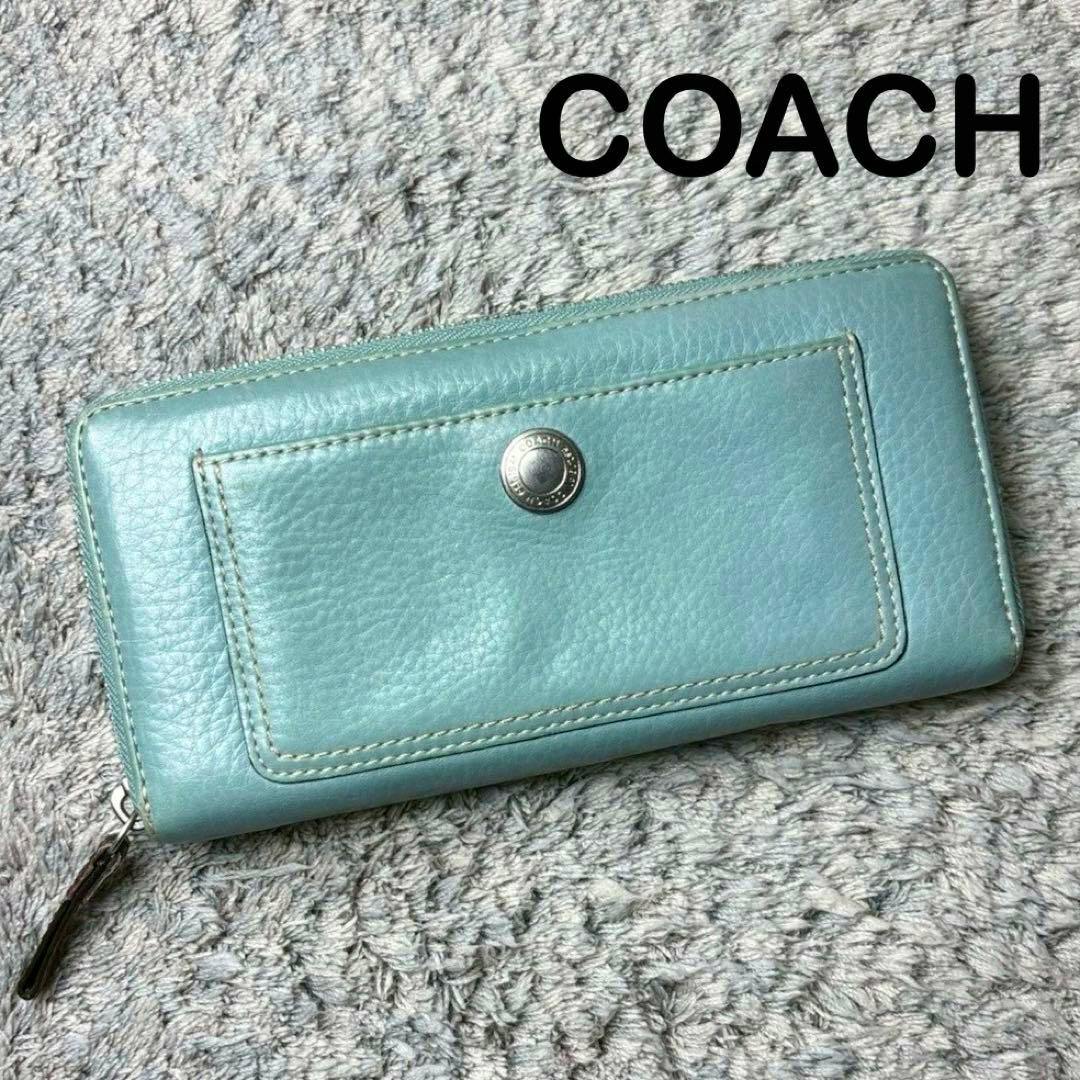 Light teal COACH long leather zip-around wallet shown flat on a gray textured surface, front pocket and zipper visible.