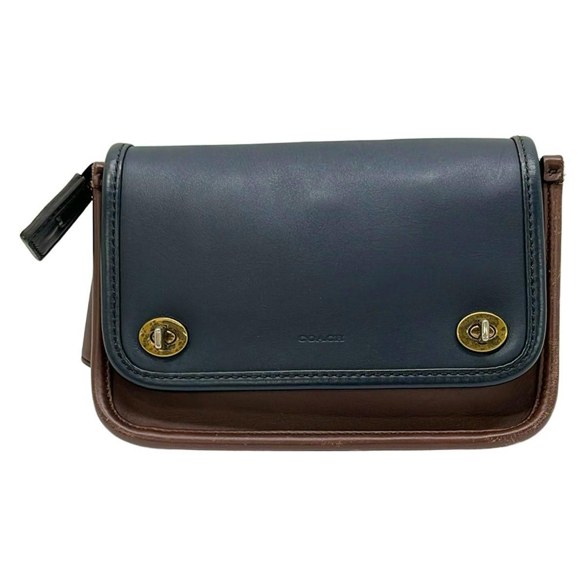 Front view of a COACH navy and dark brown leather waist pouch with twin gold turn-lock closures.