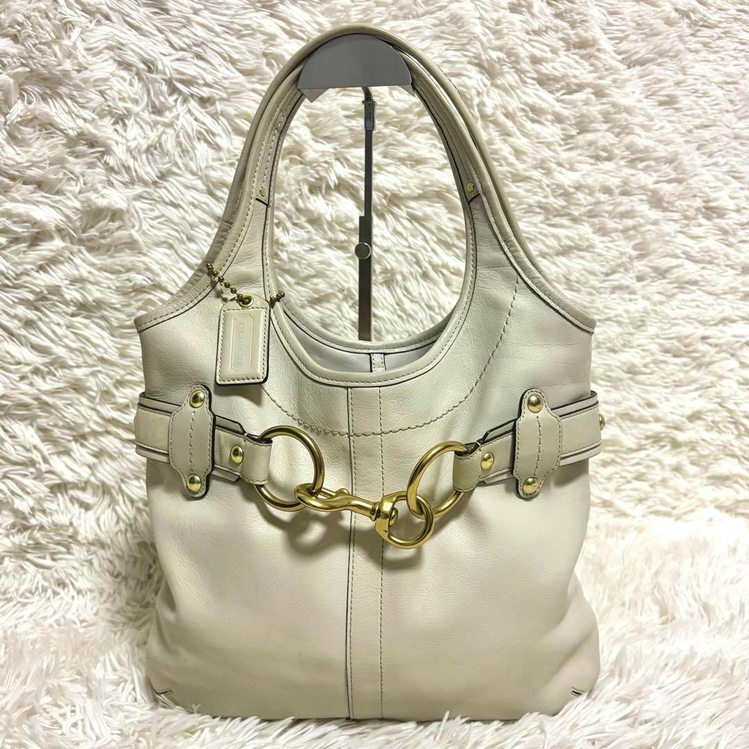 Front-facing light-colored COACH Legacy Ergo Belted Magazine Tote displayed on a textured white backdrop.