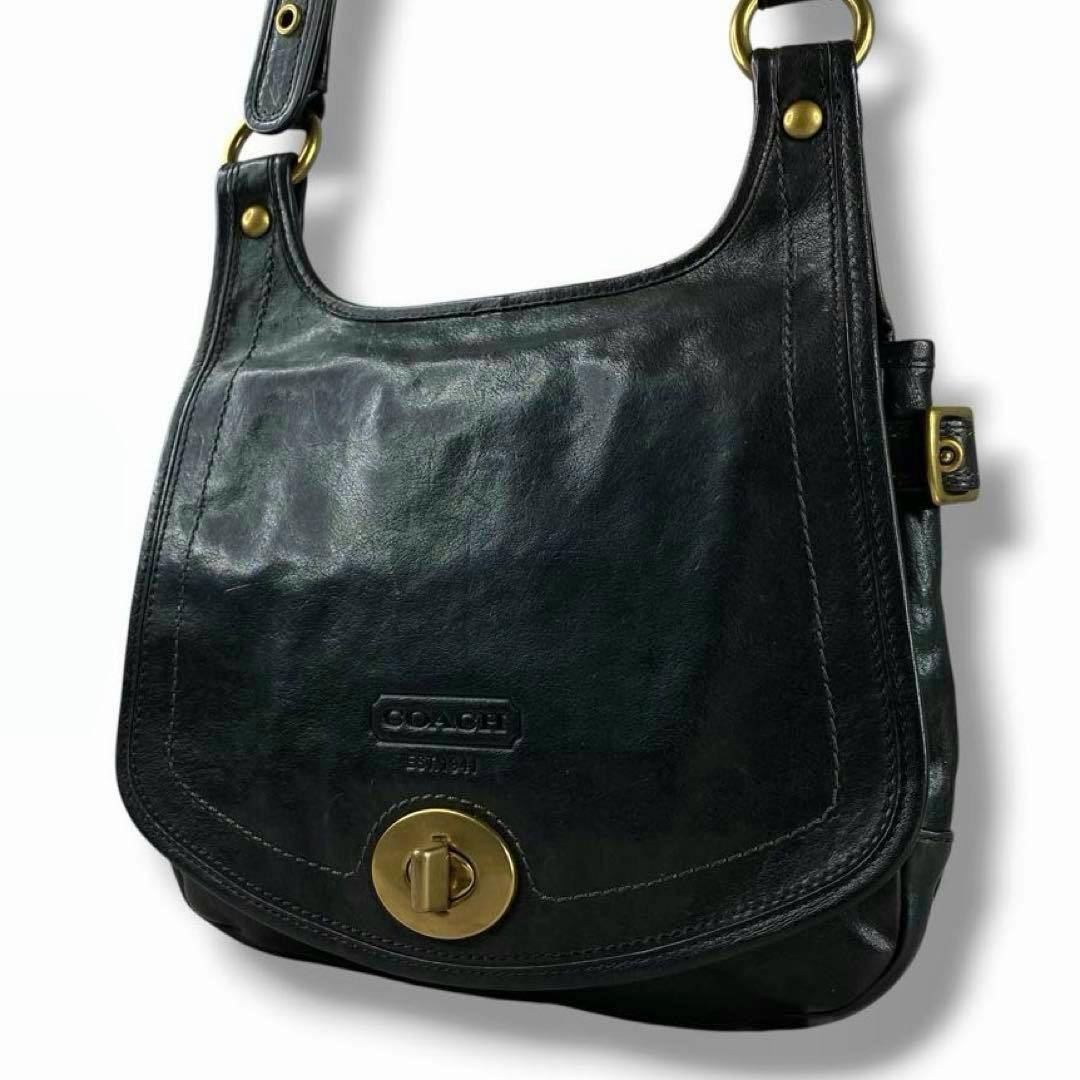 Front of a black COACH Legacy leather flap shoulder bag showing the flap, embossed COACH logo, and round brass turn-lock closure.