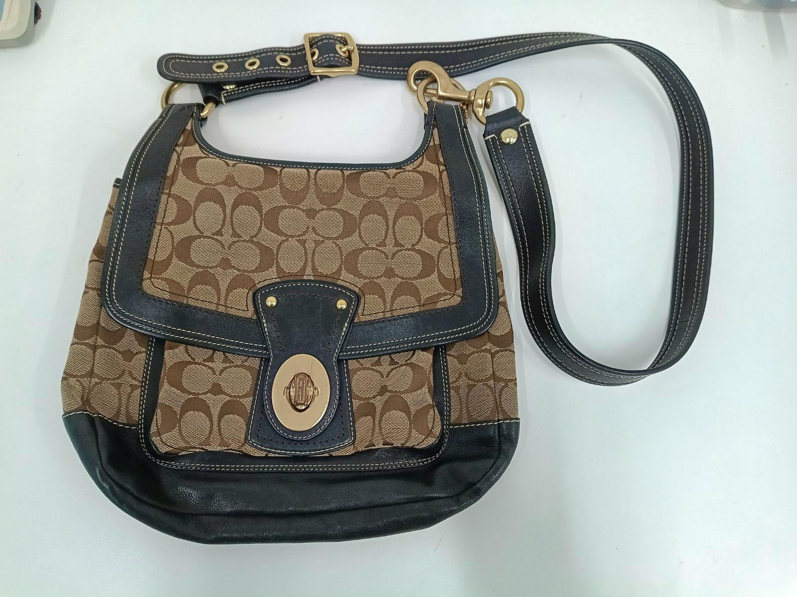 Front view of the COACH Legacy shoulder bag showing brown signature C pattern, dark leather trim, adjustable strap, and gold turn-lock closure on a white background.