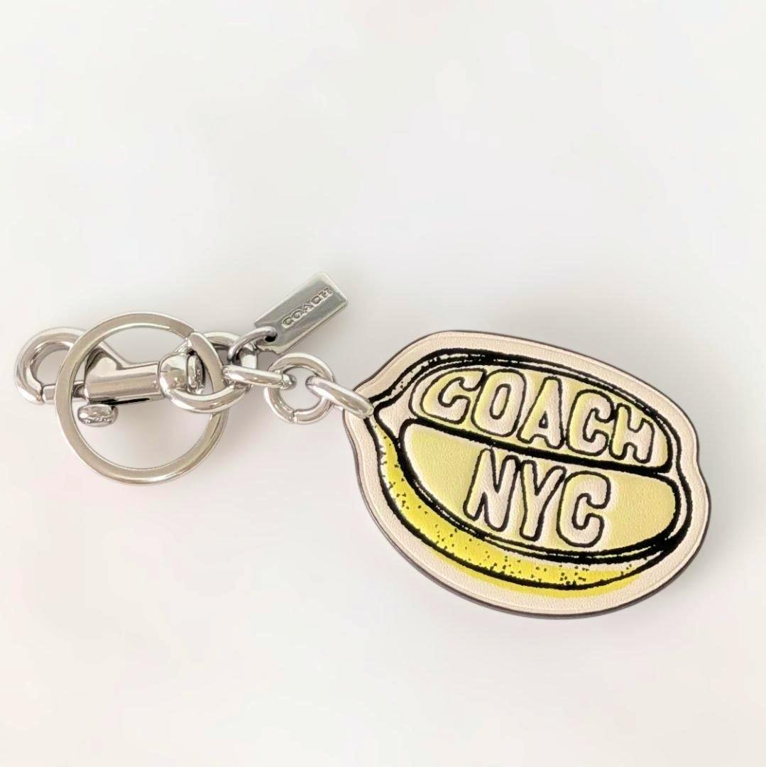 Coach lemon leather keychain showing a lemon-shaped charm stamped "COACH NYC" attached to a silver keyring on a white background.