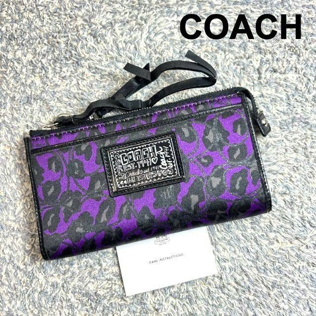 A COACH purple leopard-print long zip wristlet wallet (canvas) pictured on a textured surface with a care instructions card.