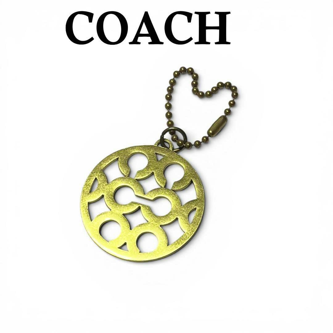Gold COACH round bag charm keychain with cutout logo pattern and beaded chain on a white background.