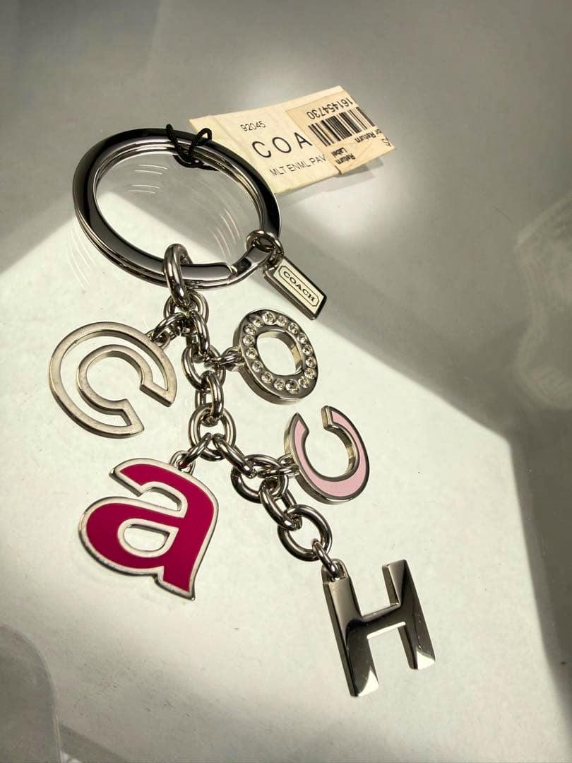 Silver COACH keyring with multicolor pastel letter charms, a rhinestone 'O' charm, and a small COACH tag.