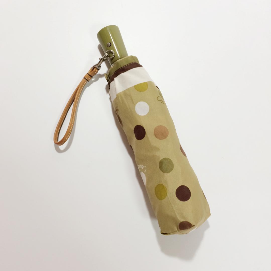 Folded beige Coach polka-dot folding umbrella in its matching sleeve with a tan wrist strap.