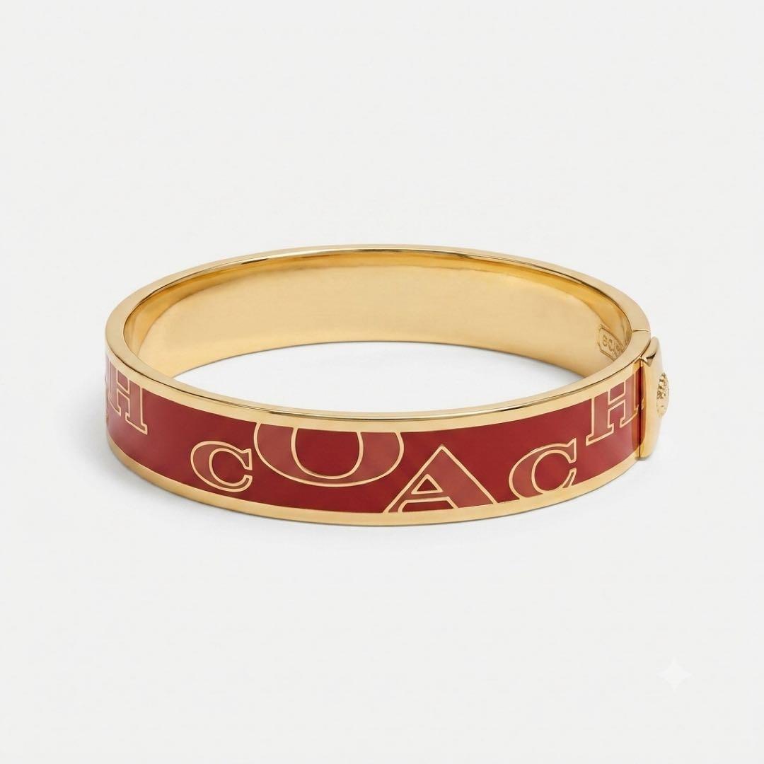 Gold-tone bangle bracelet with a red enamel band showing the COACH logo pattern.