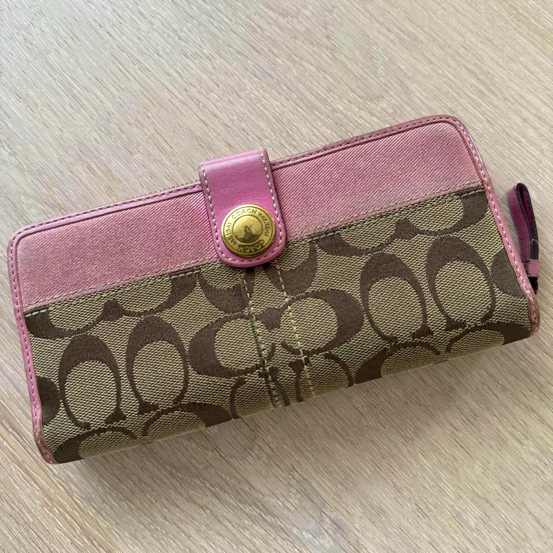 Pink and brown Coach long canvas wallet with signature logo pattern and a pink snap tab placed on a wood surface.