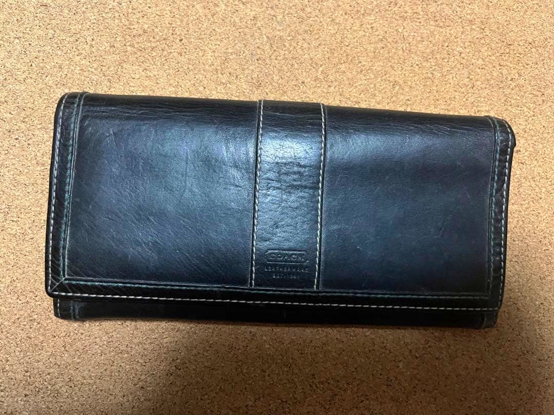 Closed black Coach long cow leather wallet placed on a cork surface.