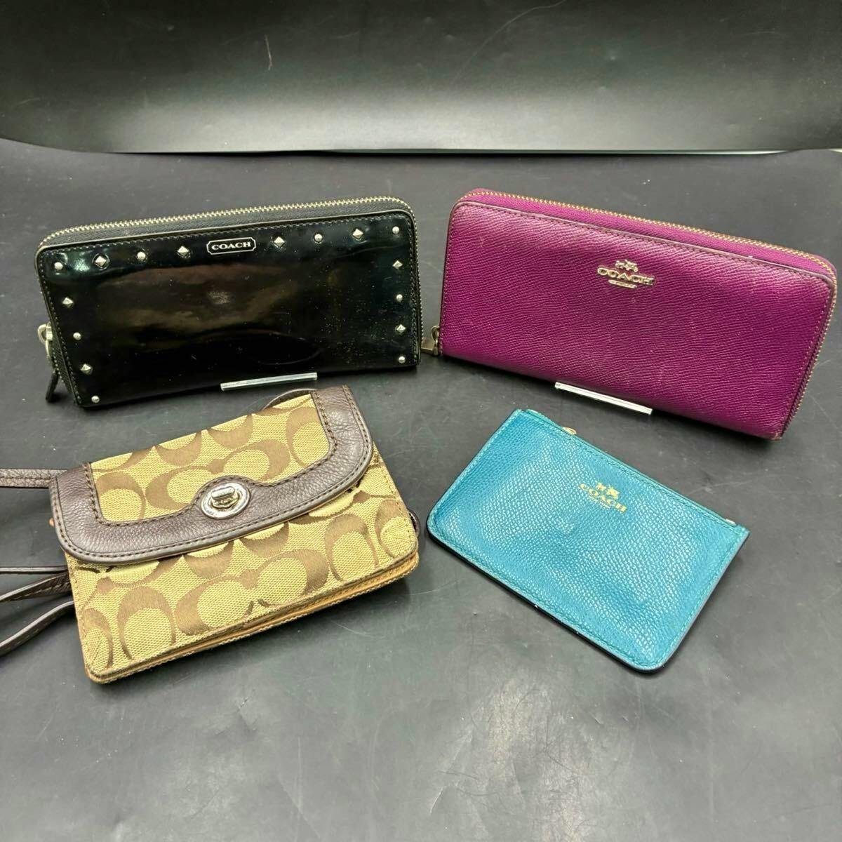 Four COACH wallets and card cases in black, purple, brown signature canvas, and teal arranged on a dark surface.