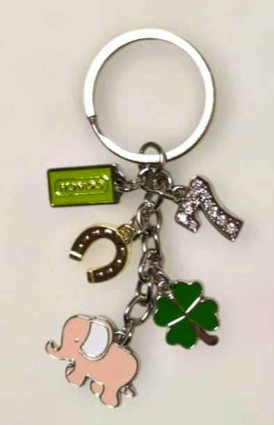 Metal bag charm key ring with a pink elephant, green four-leaf clover, horseshoe, rhinestone '7', and a small green COACH tag.