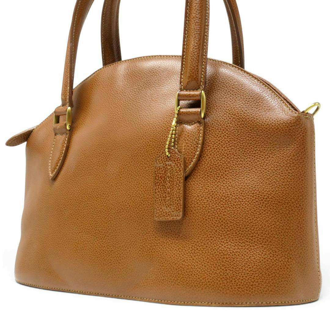 Three-quarter view of a brown Coach leather Madison handbag showing the front, handles, and a leather hang tag.