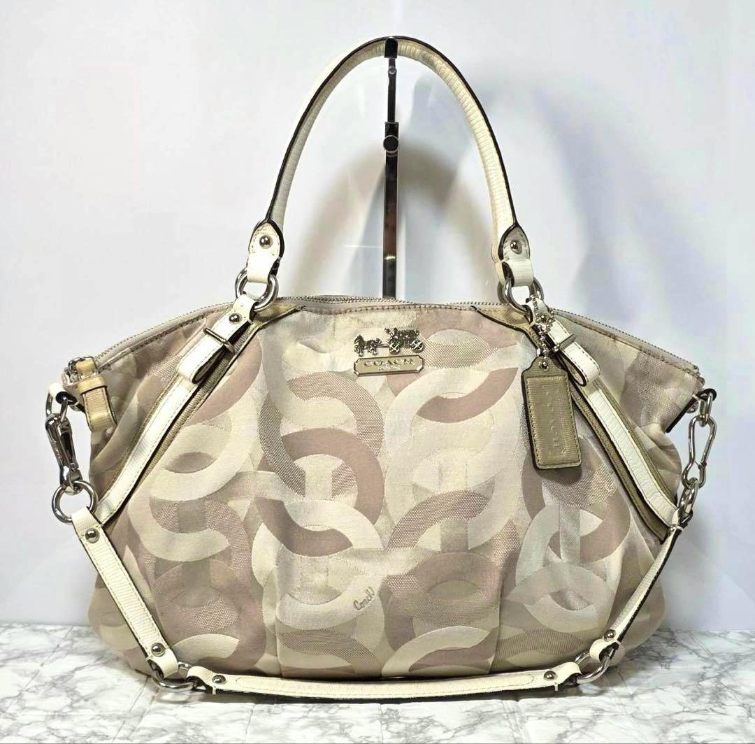 Front view of the Coach Madison Op Art 2WAY canvas bag in beige with double handles, detachable shoulder strap, and a Coach hang tag.