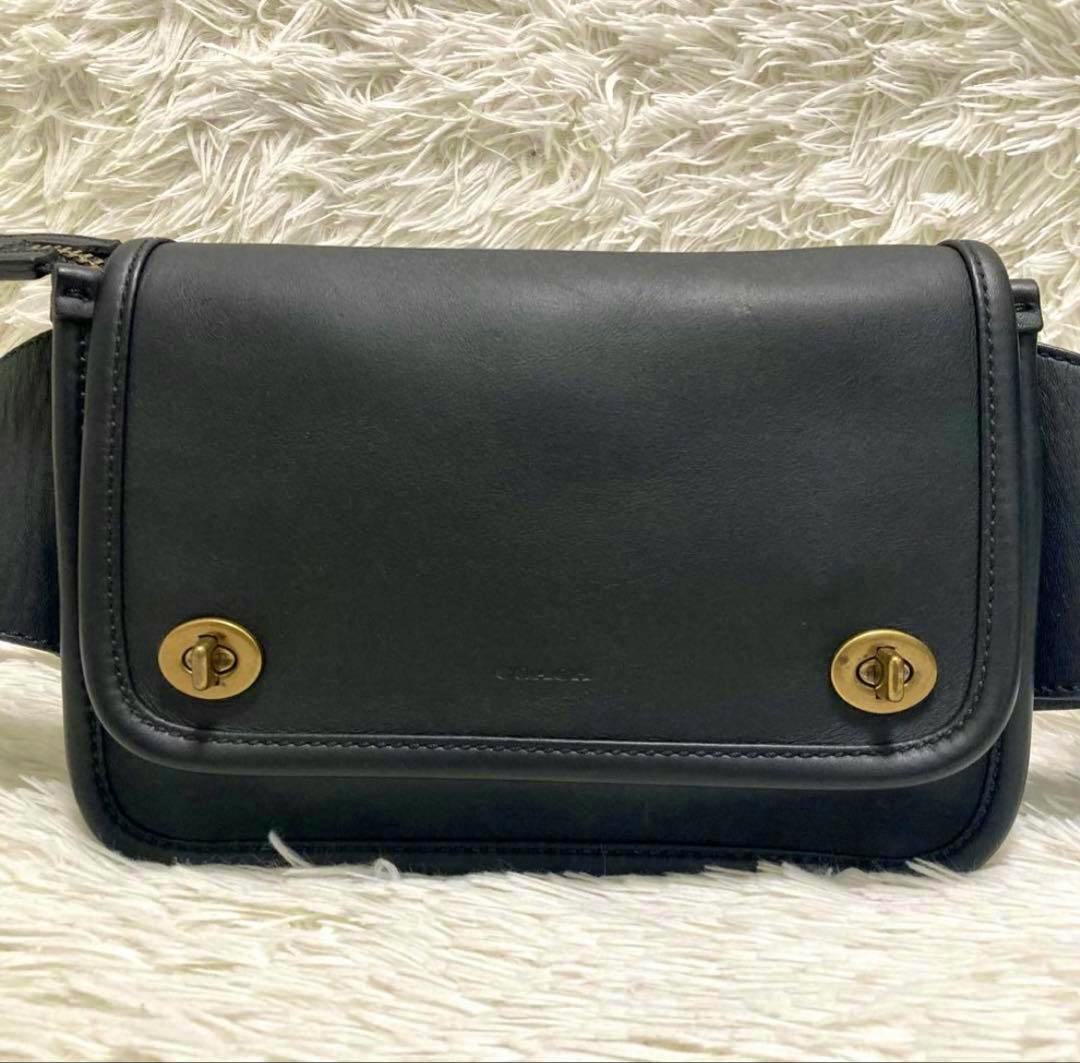 Front view of a black Coach leather body bag showing two brass turn-lock closures.