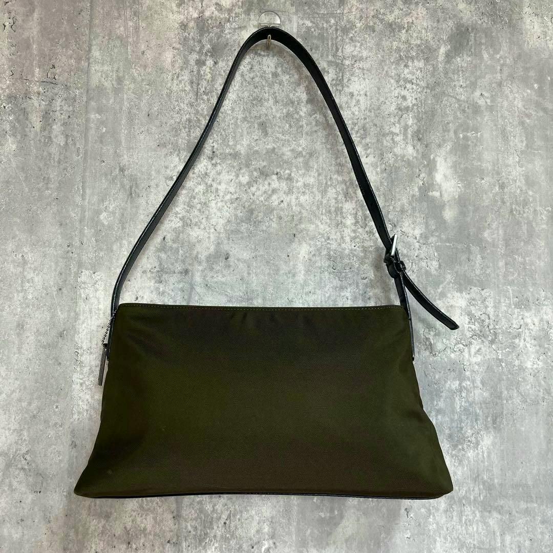 Khaki nylon COACH Mercer shoulder bag with a black leather strap hanging against a gray background.