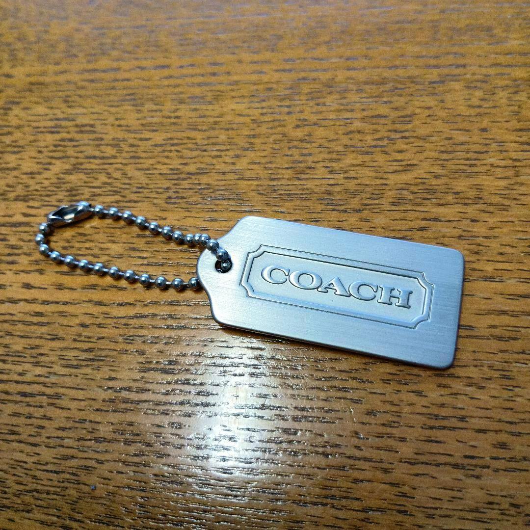 COACH metal tag charm keychain with a ball-chain lying on a wooden surface.