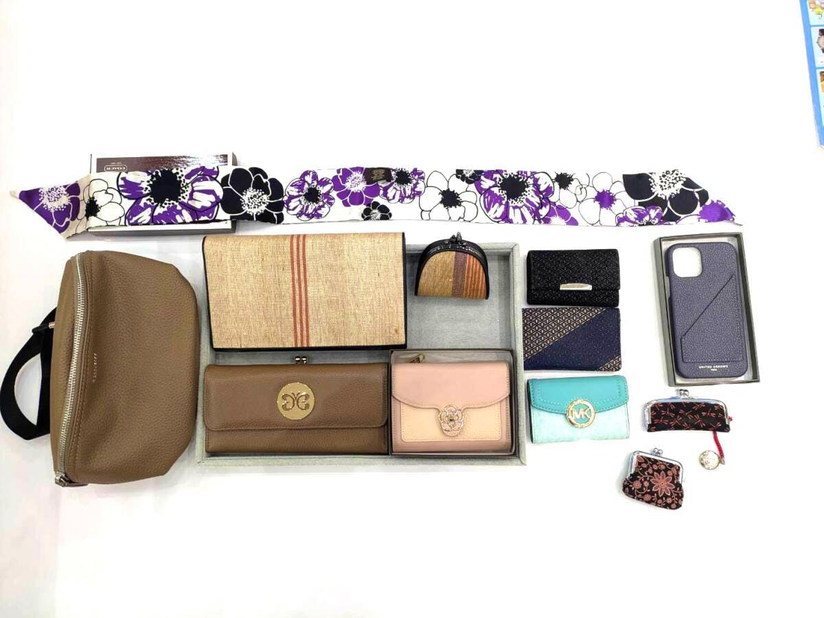 Top-down photo of assorted small leather goods and accessories on a white background, including a brown leather pouch, several wallets and coin purses, a phone case, and a floral scarf.