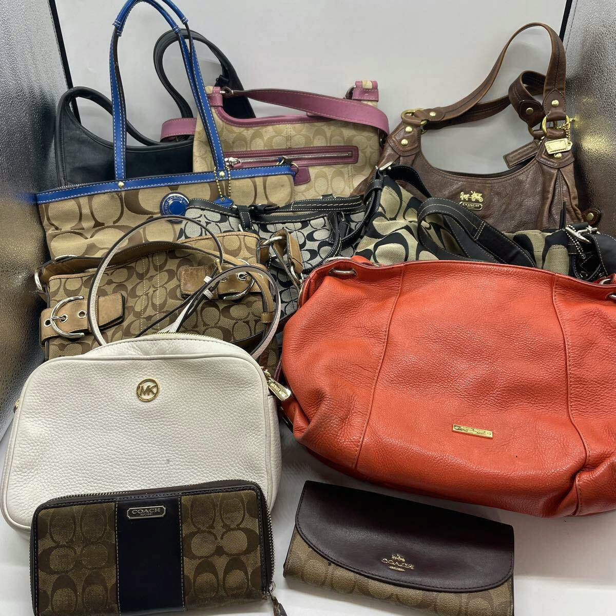 Multiple bags and wallets displayed together, including Coach canvas monogram bags and other branded handbags.
