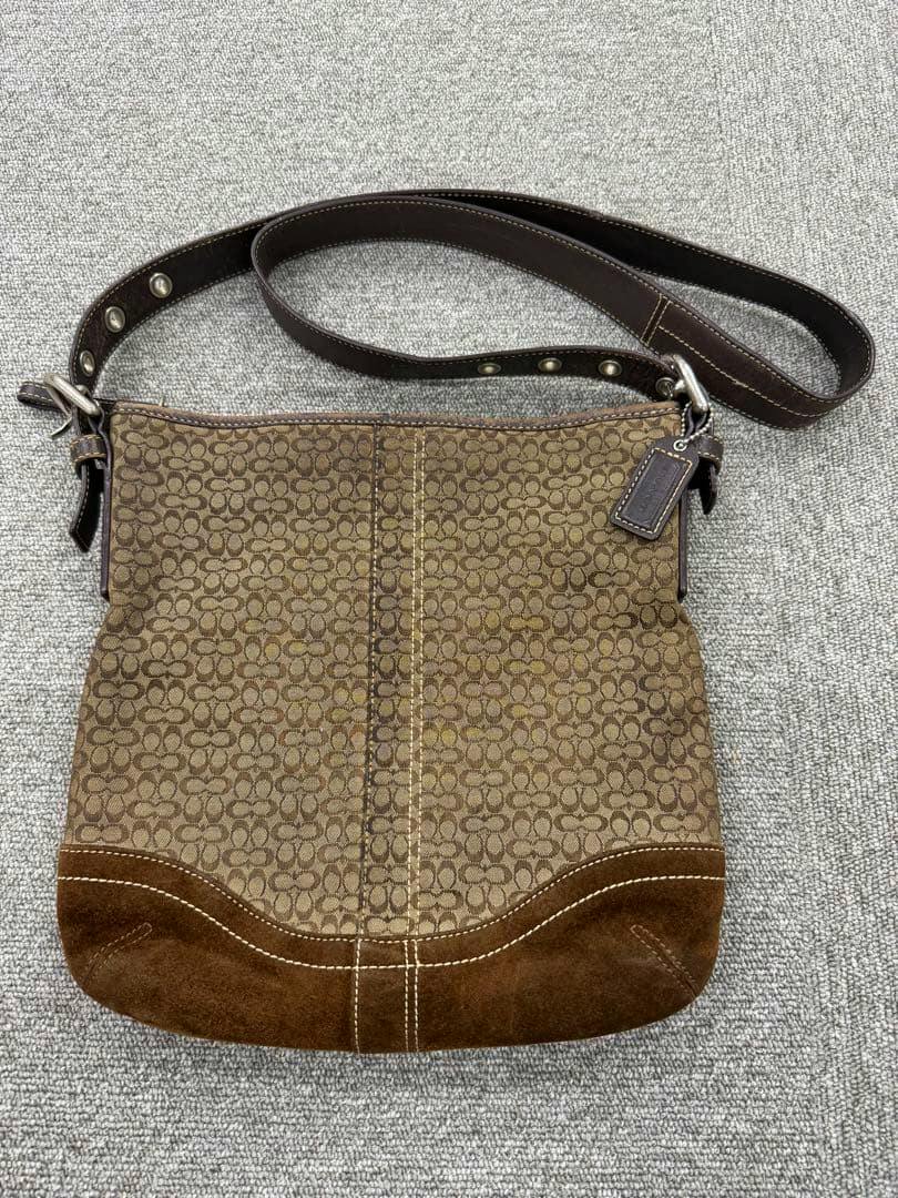 Brown COACH micro-signature canvas shoulder bag with dark leather strap and suede bottom shown flat on a gray surface.