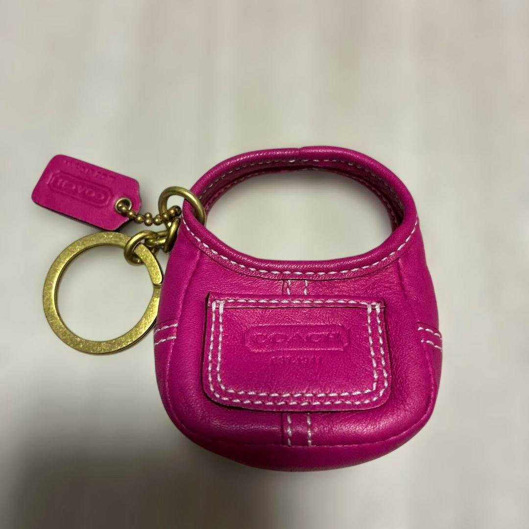 Pink COACH mini bag-shaped keychain charm with white stitching and an attached gold-tone key ring on a light background.