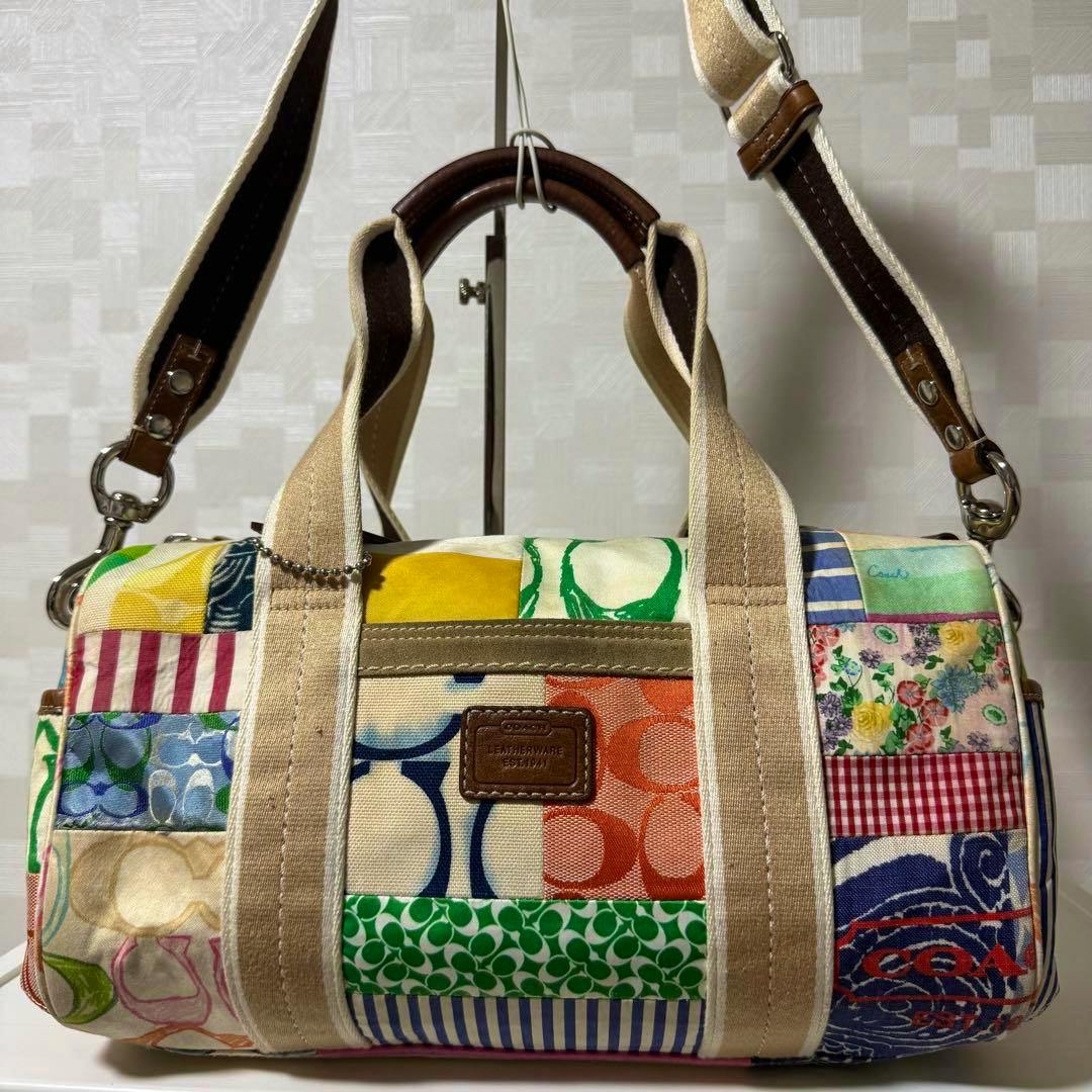 Front view of the COACH Mini Bostonbag 2way patchwork bag showing patchwork fabric panels, canvas vertical straps, leather top handles, and an adjustable shoulder strap.