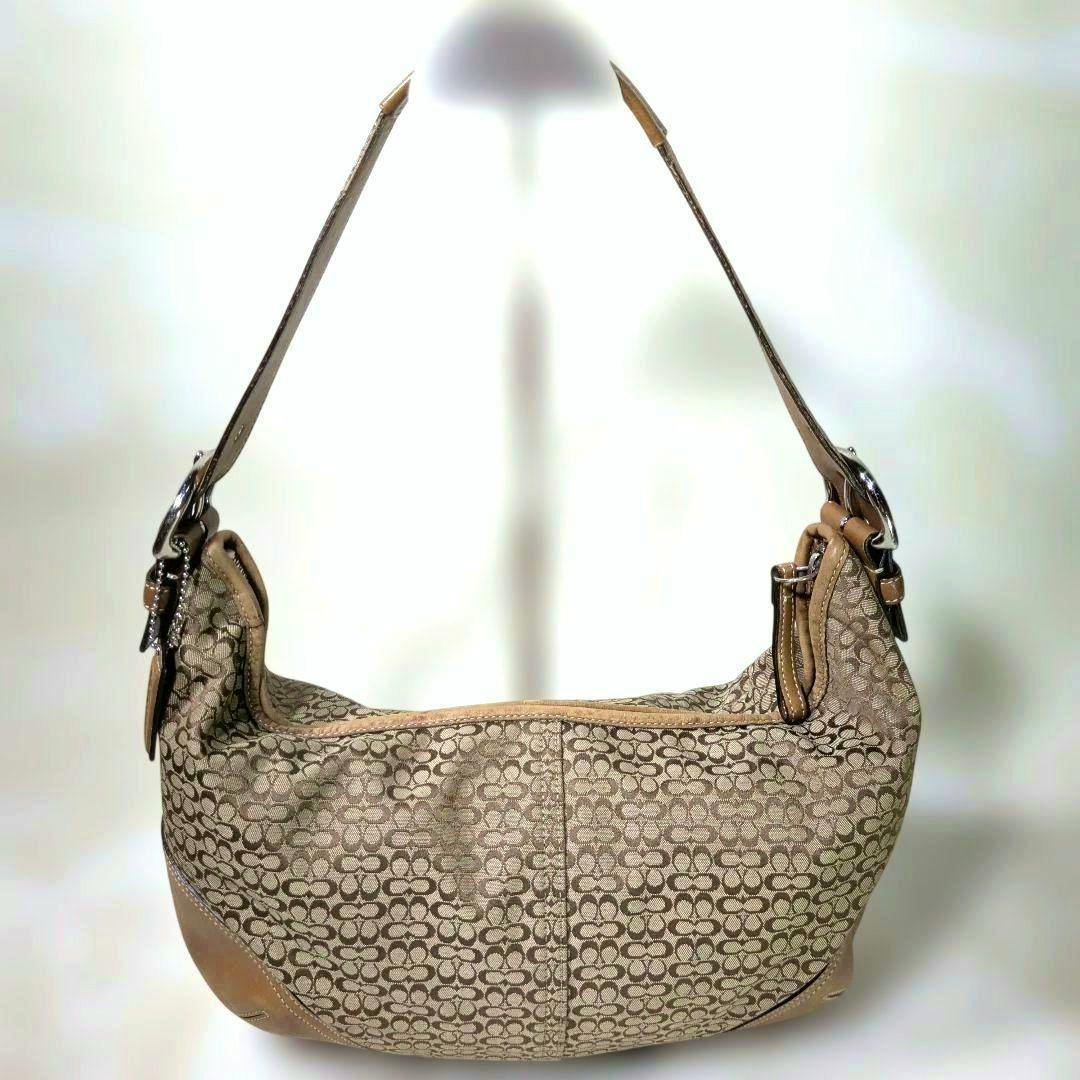 Front view of a COACH one-shoulder canvas bag with the signature pattern and leather trim hanging by its strap.