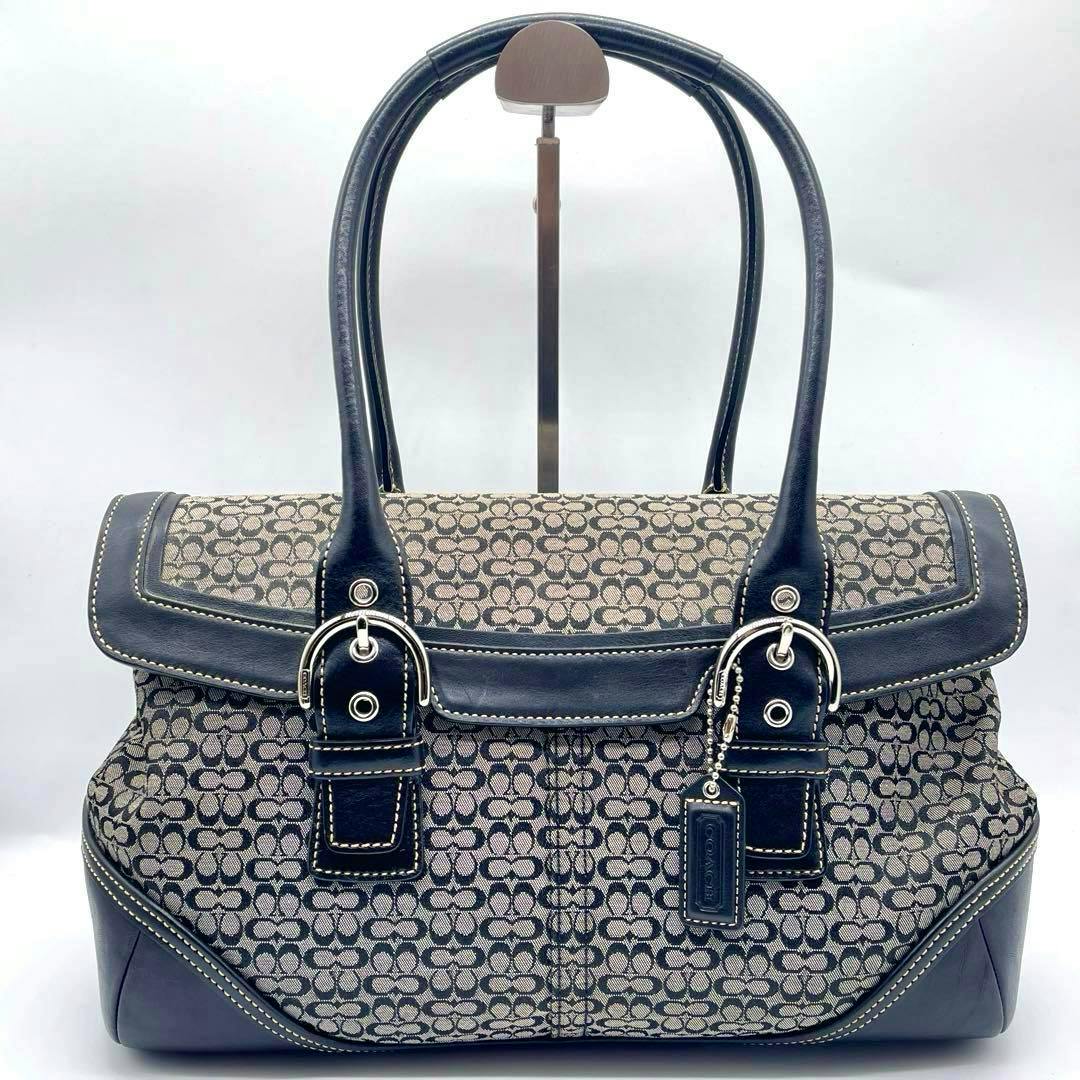 Front view of the COACH mini signature flap satchel handbag showing logo canvas, dark leather trim, double handles, buckle hardware, and a Coach hang tag.
