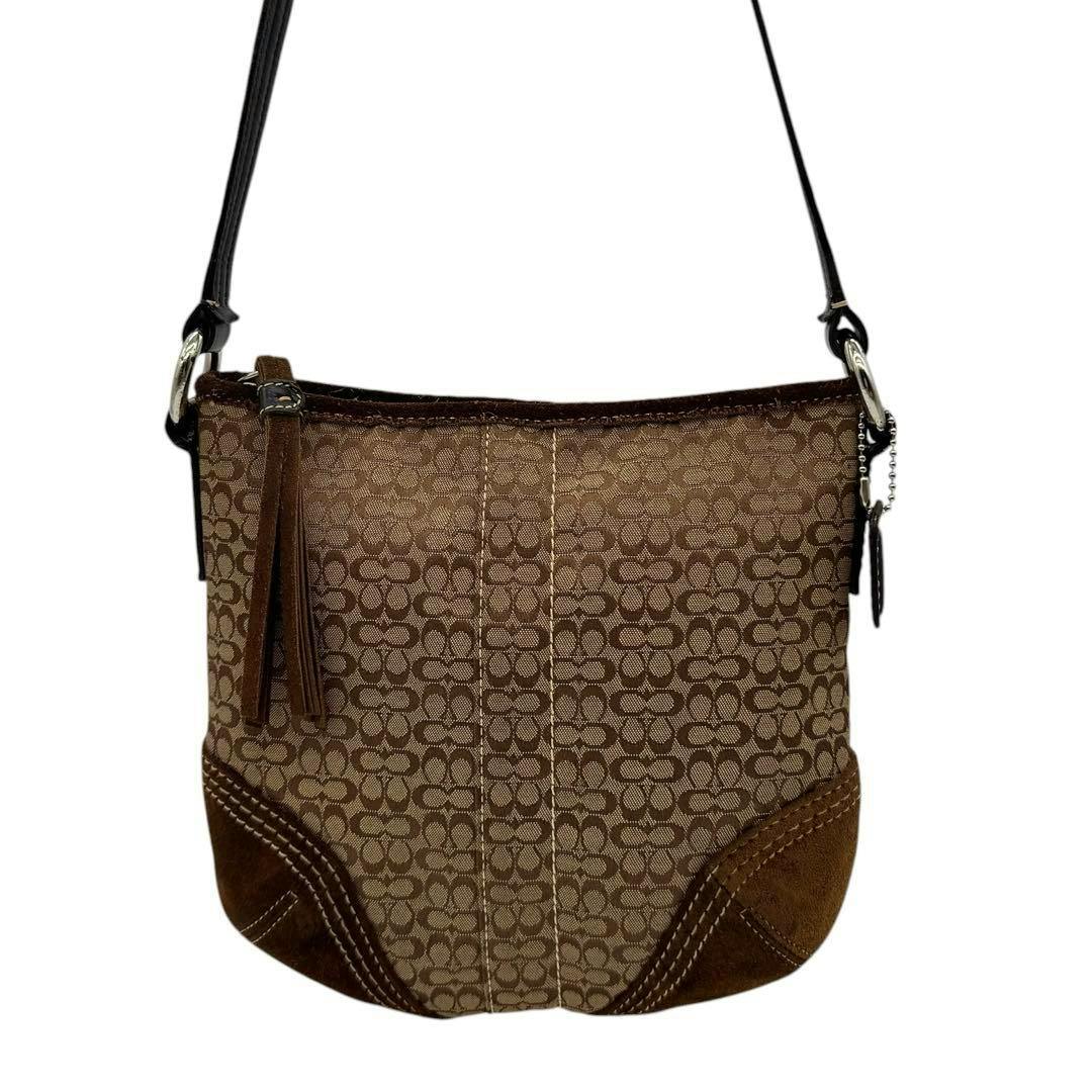 Brown Coach mini shoulder bag in signature monogram canvas with suede corner accents hanging by its strap.