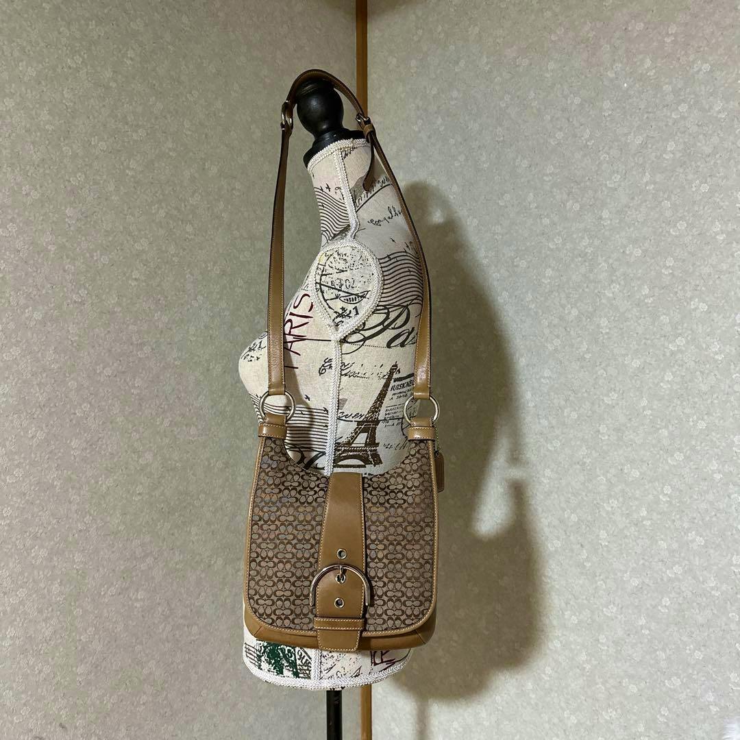 Brown Coach mini shoulder bag with signature canvas pattern and buckle hanging on a dress form.