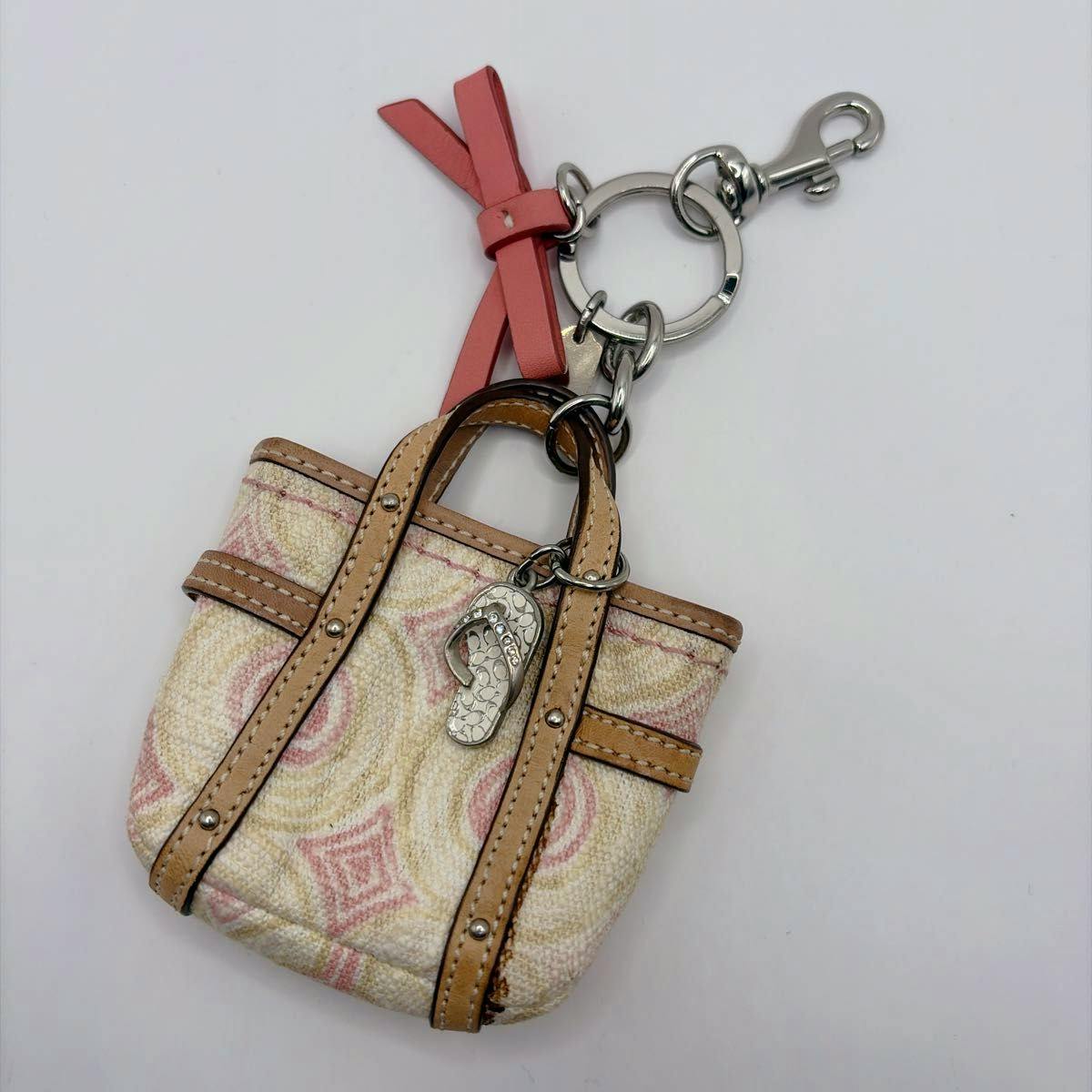 A Coach mini tote bag charm keychain with a pink ribbon, leather trim, and a small metal flip-flop charm attached to a keyring.