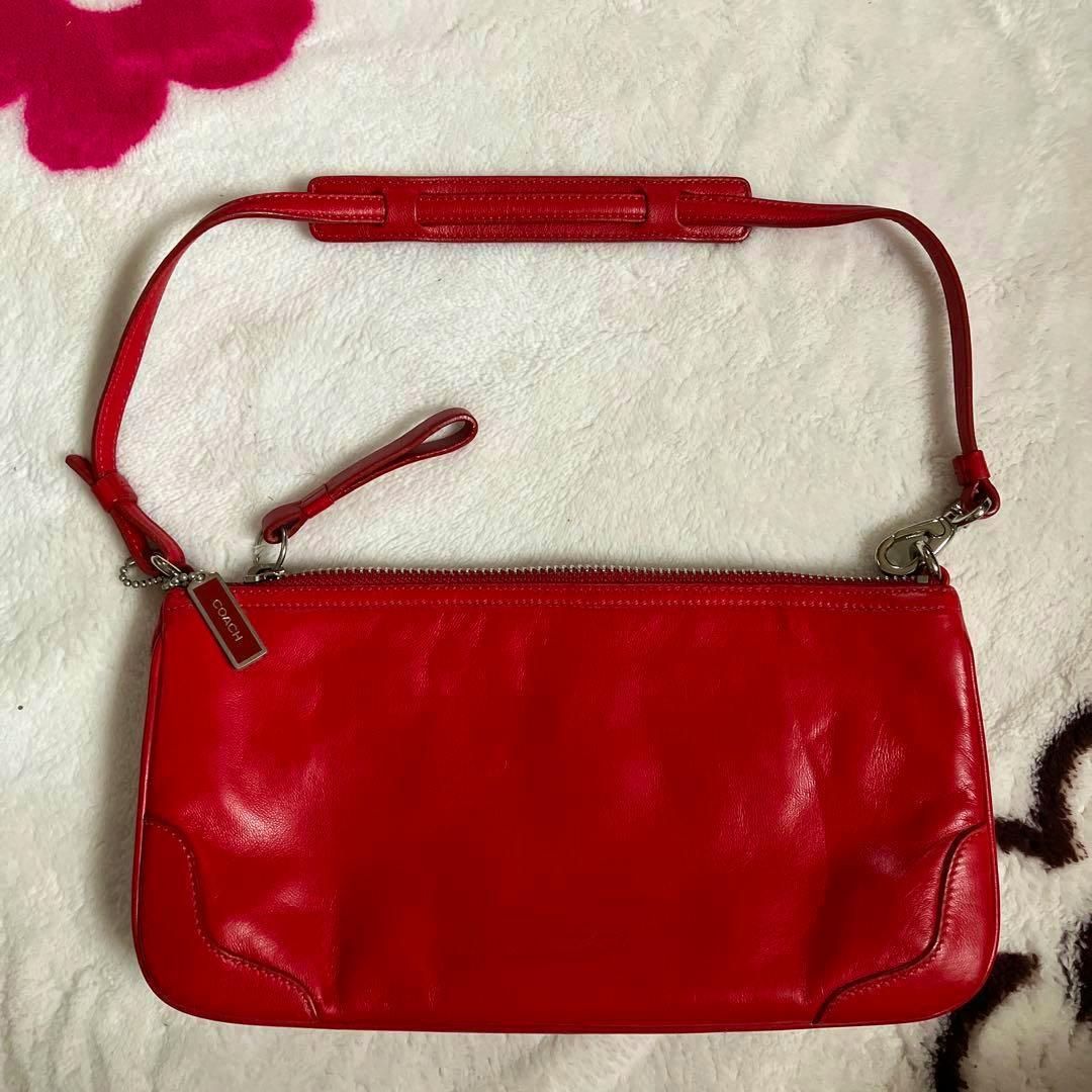 Front view of the red COACH mini tote pouch bag with strap displayed on a white textured surface.