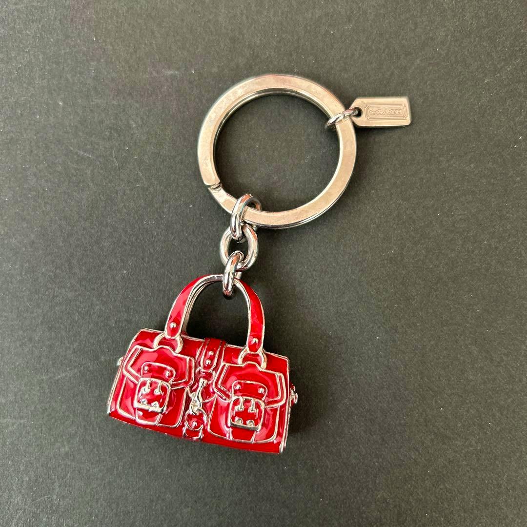 Red miniature handbag keychain with a silver key ring and small rectangular tag on a dark background.