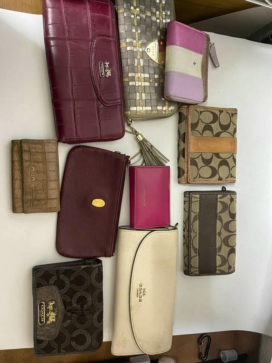 Overhead photo of ten wallets and small purses of various colors and patterns laid out on a white surface.