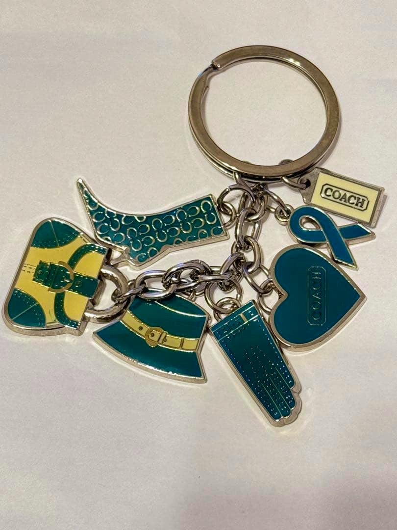 Front view of the COACH multi-motif bag charm keyring showing teal and yellow enamel charms attached to a metal ring.